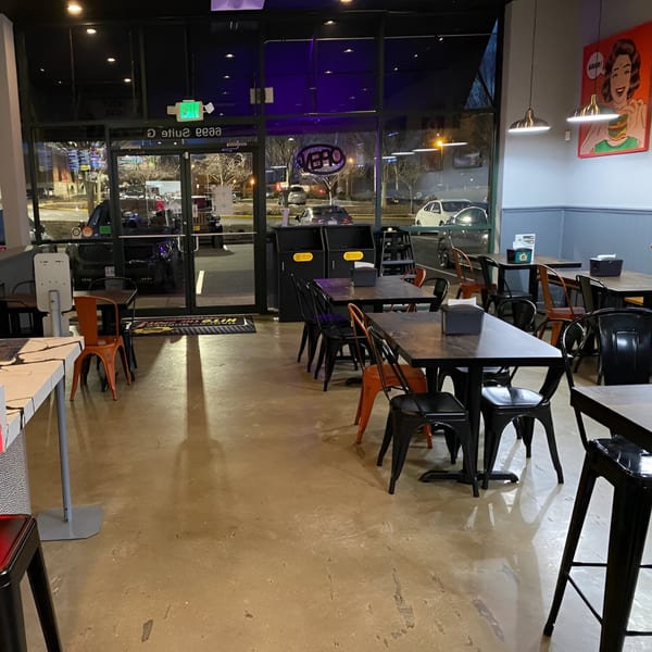 Empty Hangry Burger dining room with black and orange chairs, dark tables, and a pop art burger poster.