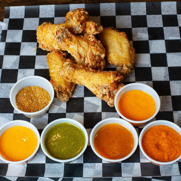 Crispy fried chicken wings with various dipping sauces and a spice rub on checkered paper.