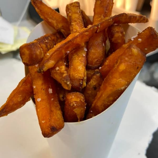 Crispy, golden-brown sweet potato fries with visible salt crystals, served in a white paper cup.