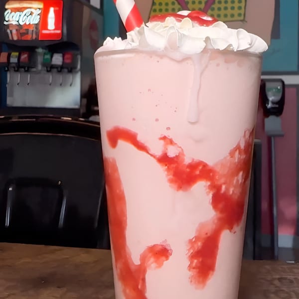 A strawberry milkshake with whipped cream, a cherry, and a red and white striped straw.