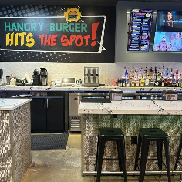 Hangry Burger bar area with a large sign, liquor bottles, and bar stools.