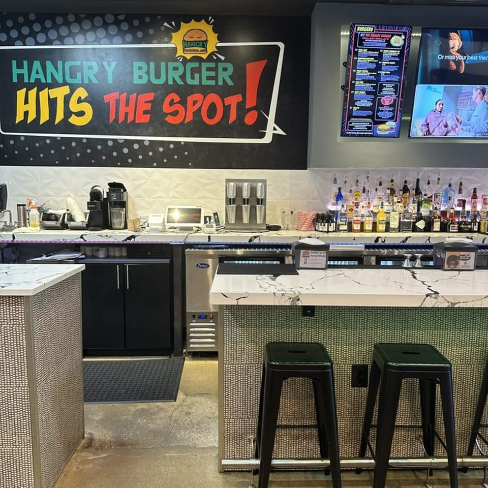 Hangry Burger bar area with a large sign, liquor bottles, and bar stools.