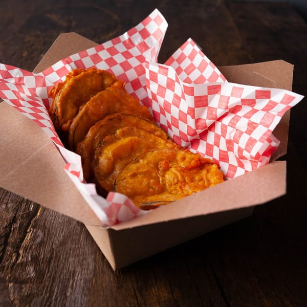 Golden-brown fried pickles in a cardboard box with red and white checkered paper.