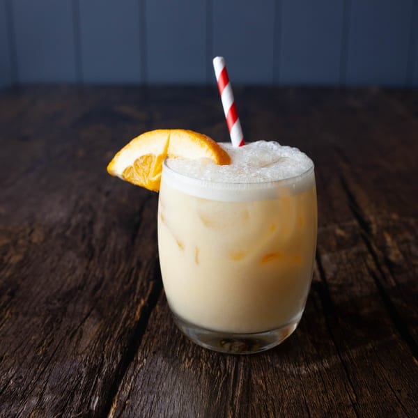 Creamy orange drink with a red and white striped straw and an orange slice garnish.