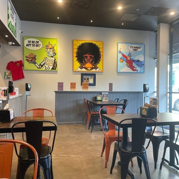 Interior of Hangry Burger with colorful pop art, dark tables, and orange and black chairs.