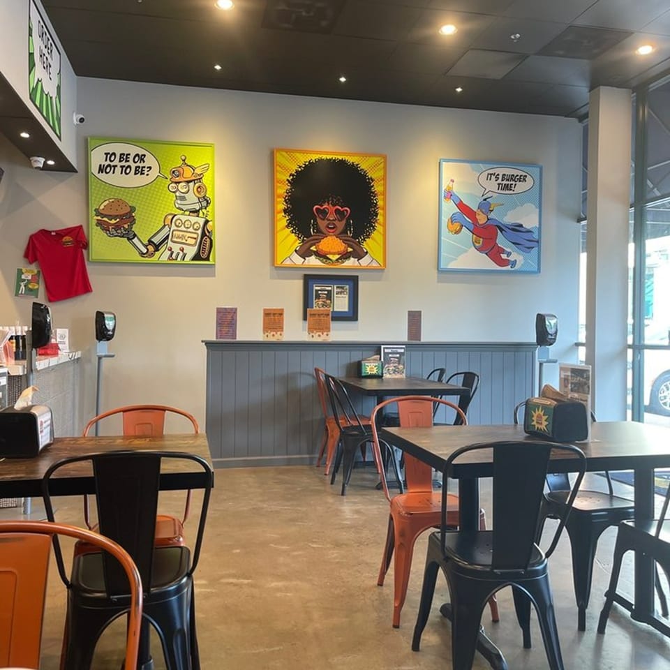 Interior of Hangry Burger with colorful pop art, dark tables, and orange and black chairs.
