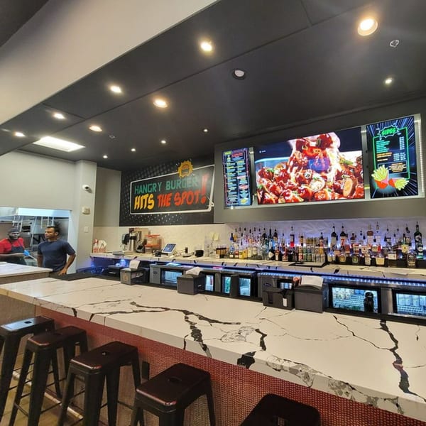 Hangry Burger restaurant interior with a long bar, bar stools, and menu screens displaying food.