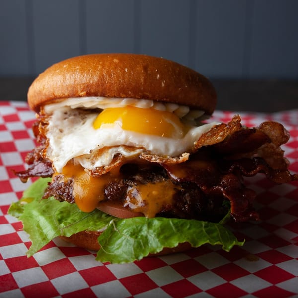 Hangry Burger's bacon cheeseburger with a fried egg and lettuce on red and white checkered paper.