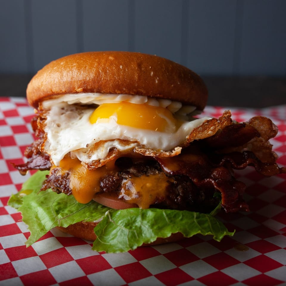Hangry Burger's bacon cheeseburger with a fried egg and lettuce on red and white checkered paper.