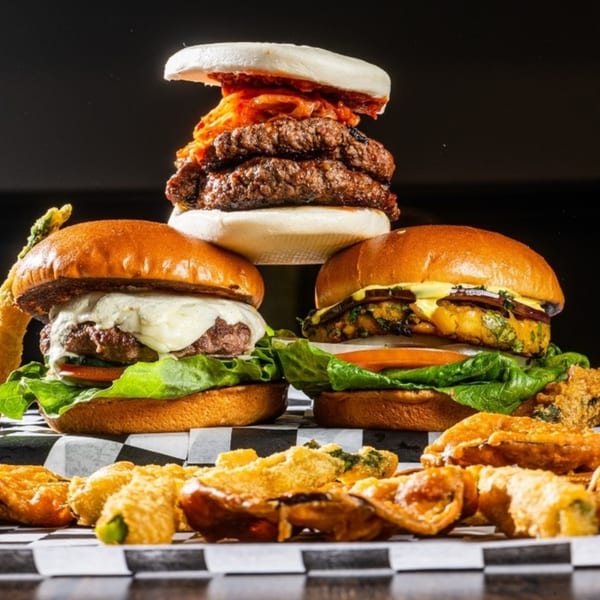 Three Hangry Burger creations: a kimchi bao burger, a cheeseburger, and a veggie burger with fried sides.