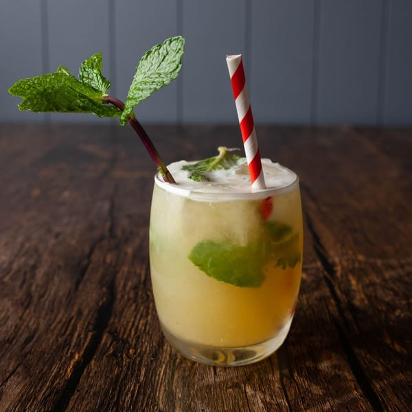 A refreshing mojito drink with mint leaves and a red and white striped straw on a wooden table.