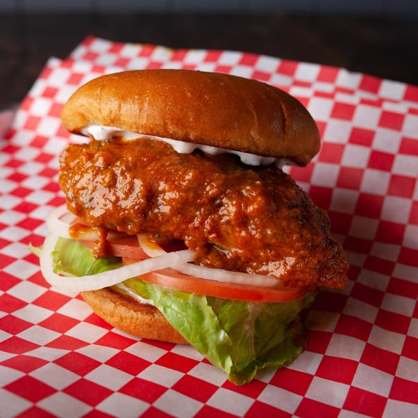 Hangry Burger's spicy chicken sandwich with lettuce, tomato, and onion on red checkered paper.