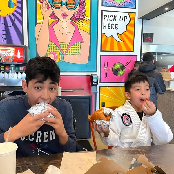 Two boys eating burgers and chicken in a vibrant Hangry Burger restaurant with pop art decor.